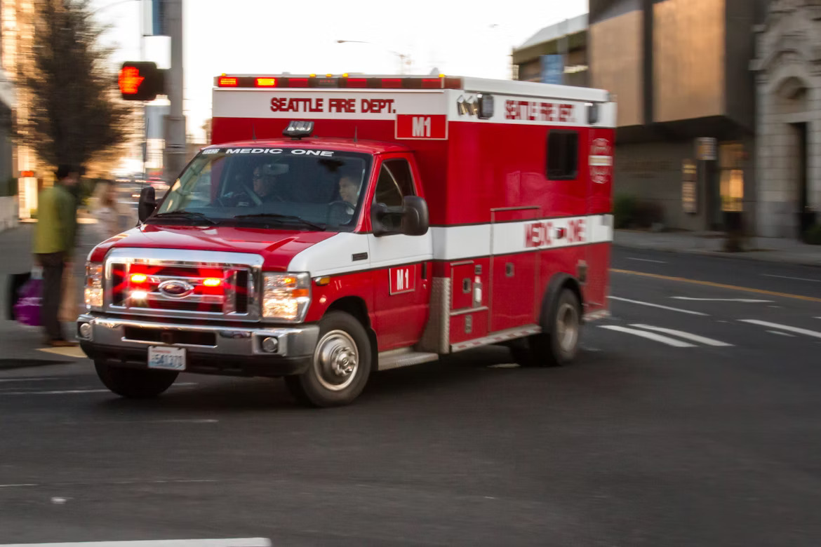 An ambulance with lights flashing makes a right turn in an intersection. Find EMT gift ideas at Army Surplus World.