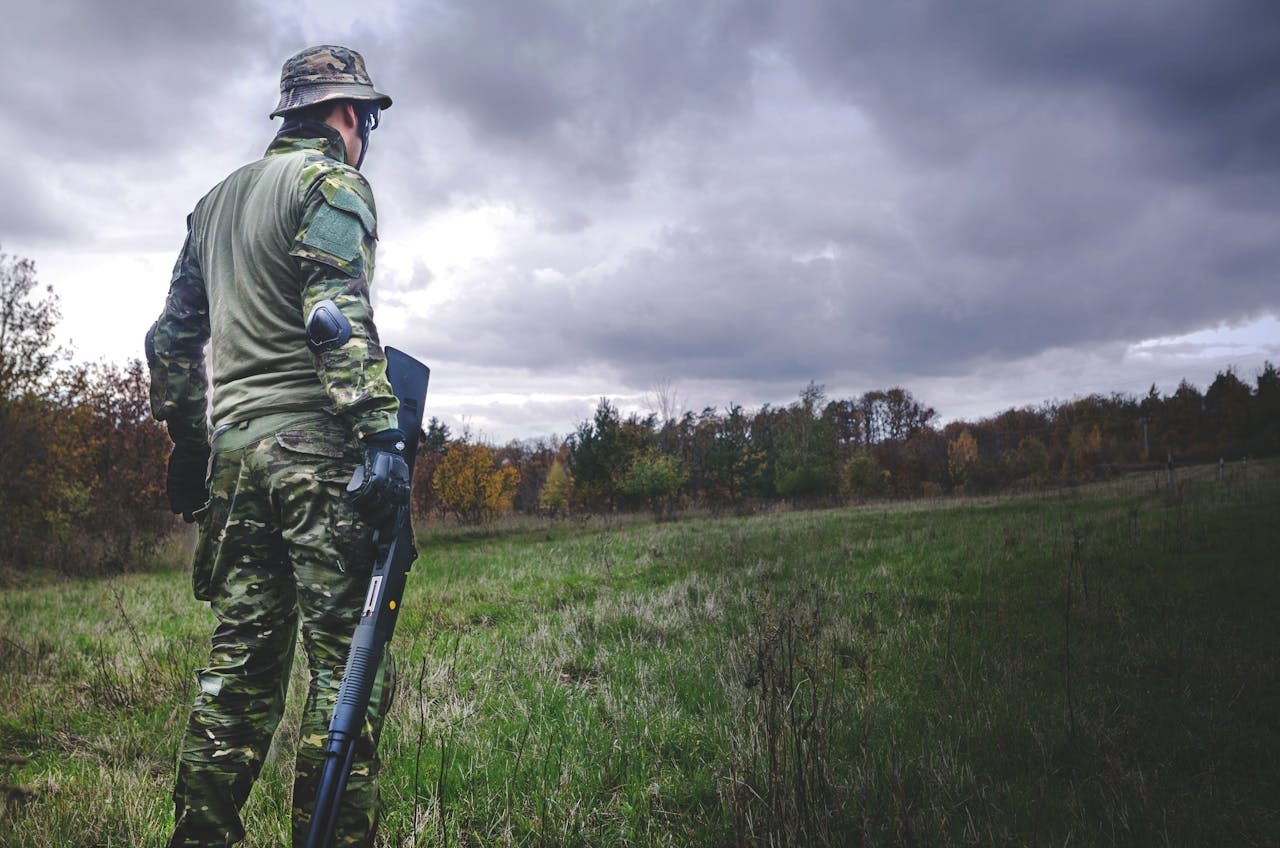 Man in camouflage clothing and elbow pads holding hunting rifle