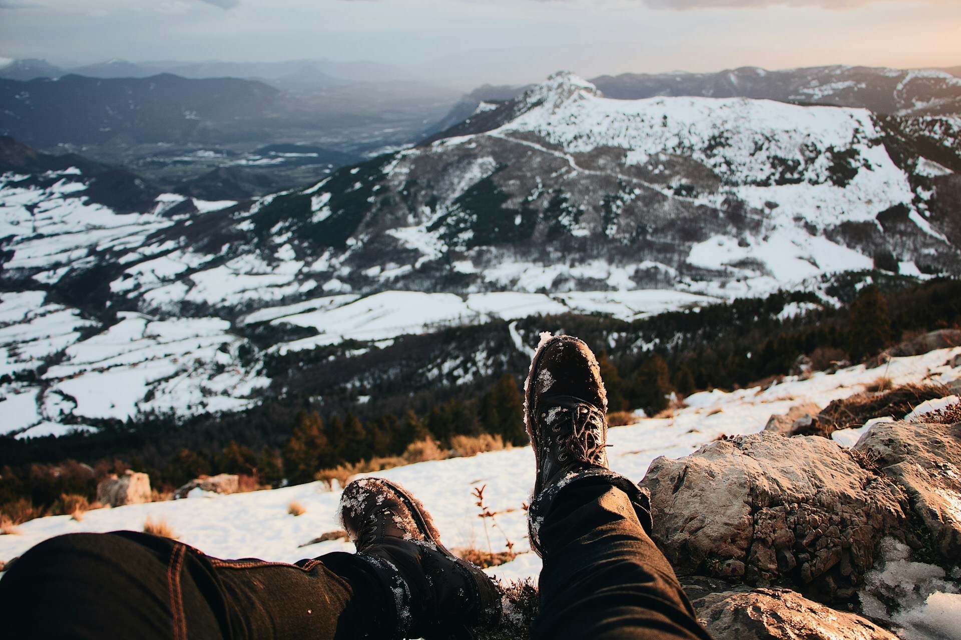 person in boots sitting on snowy mountain