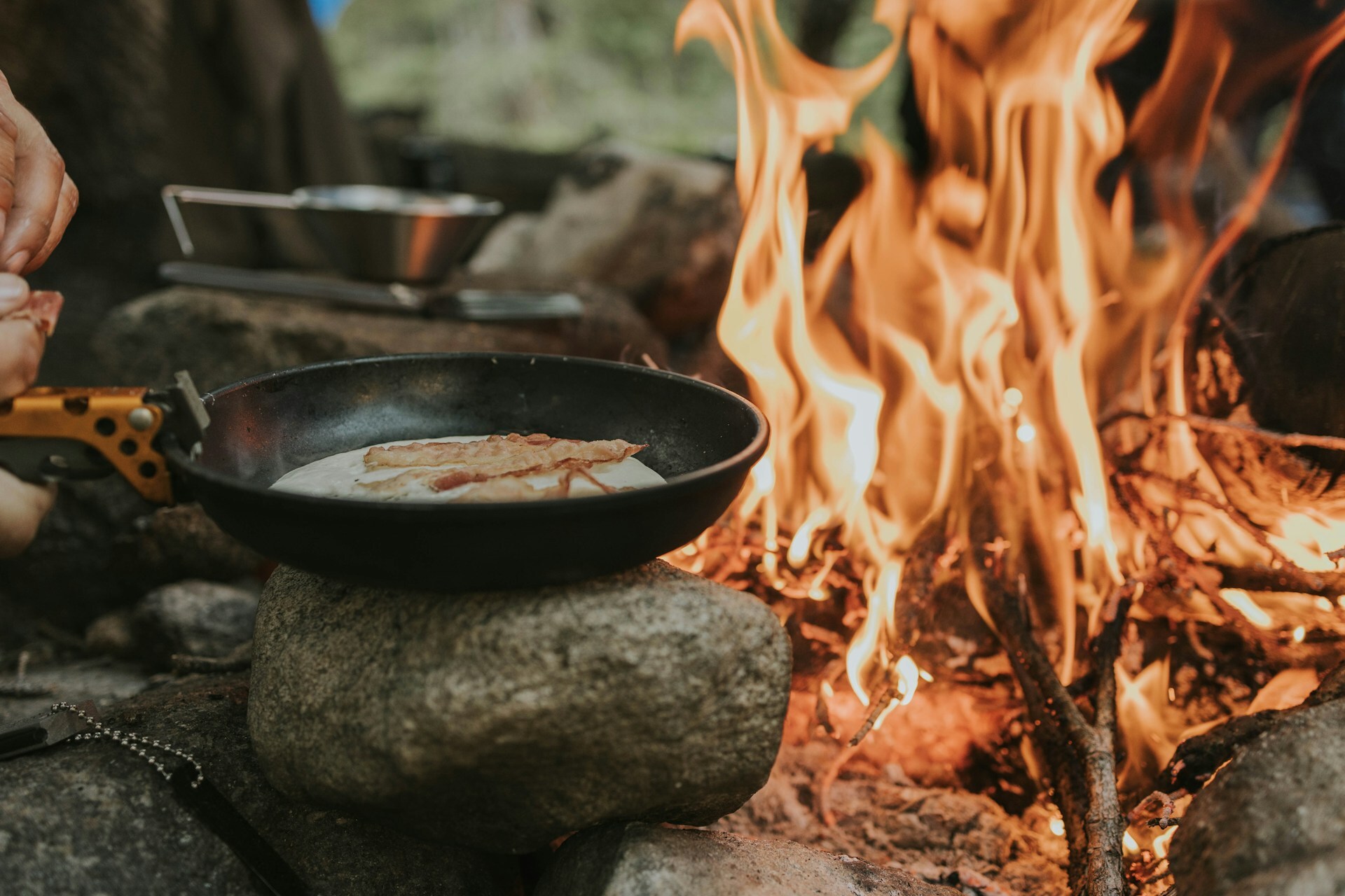 A person cooking food over a campfire A person cooking food over a campfire