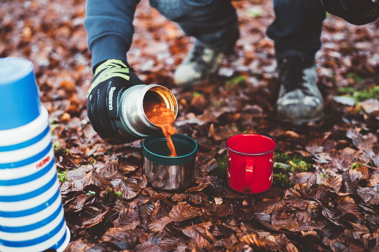 Person pouring food from thermos into cup while camping.